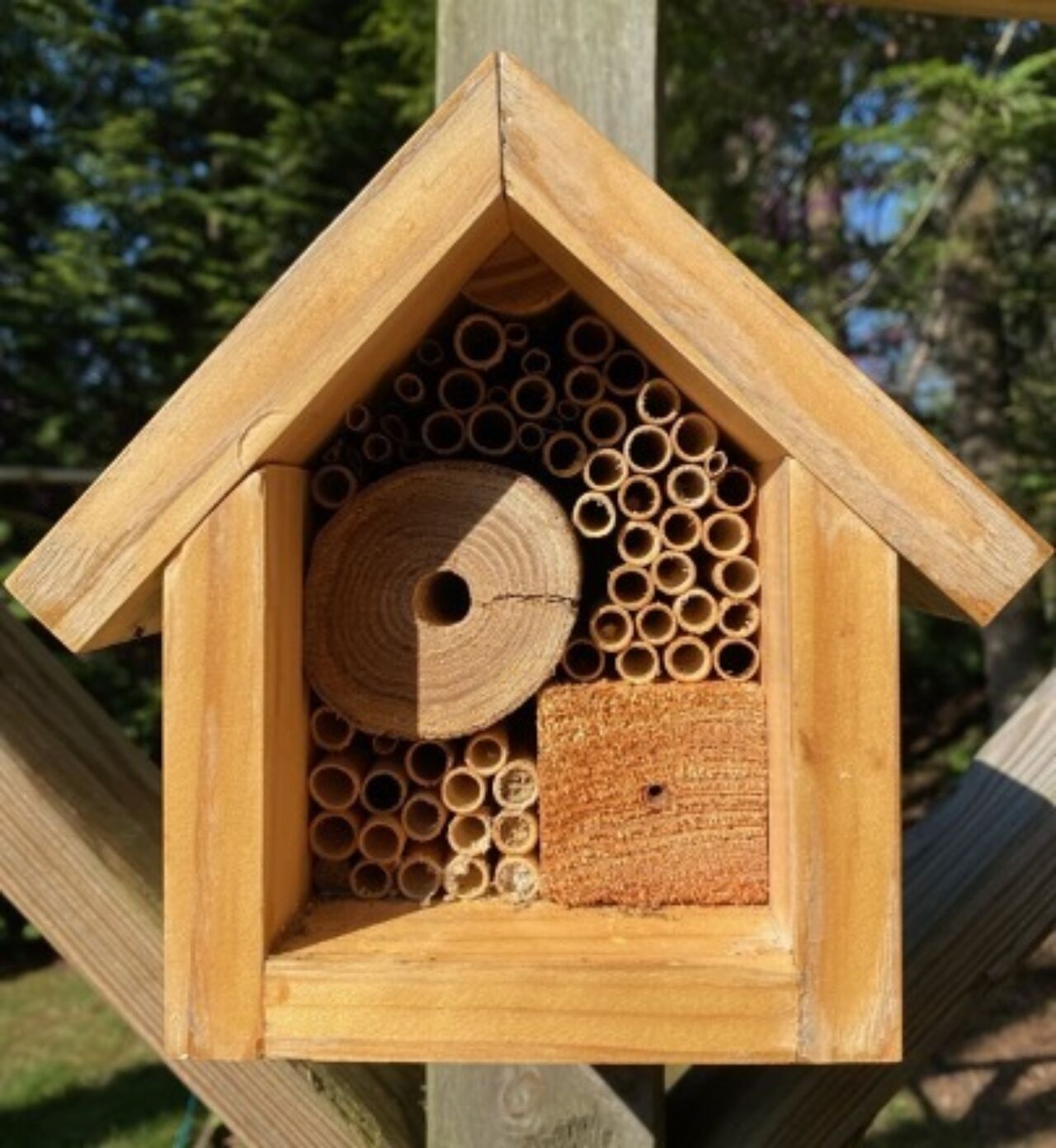 a small wooden bee hotel, about 8 inches tall filled with empty tubes and drilled wood blocks in a home garden