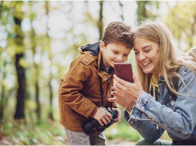 Photo of a parent and child exploring nature together, looking at plant information on a cell phone.