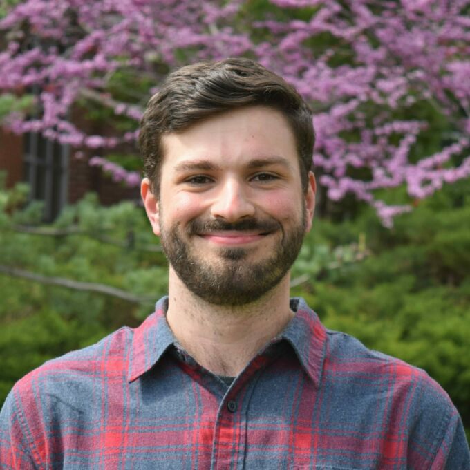 Headshot of Orion Pizzini taken outside in front of a blooming pink Eastern Redbud tree