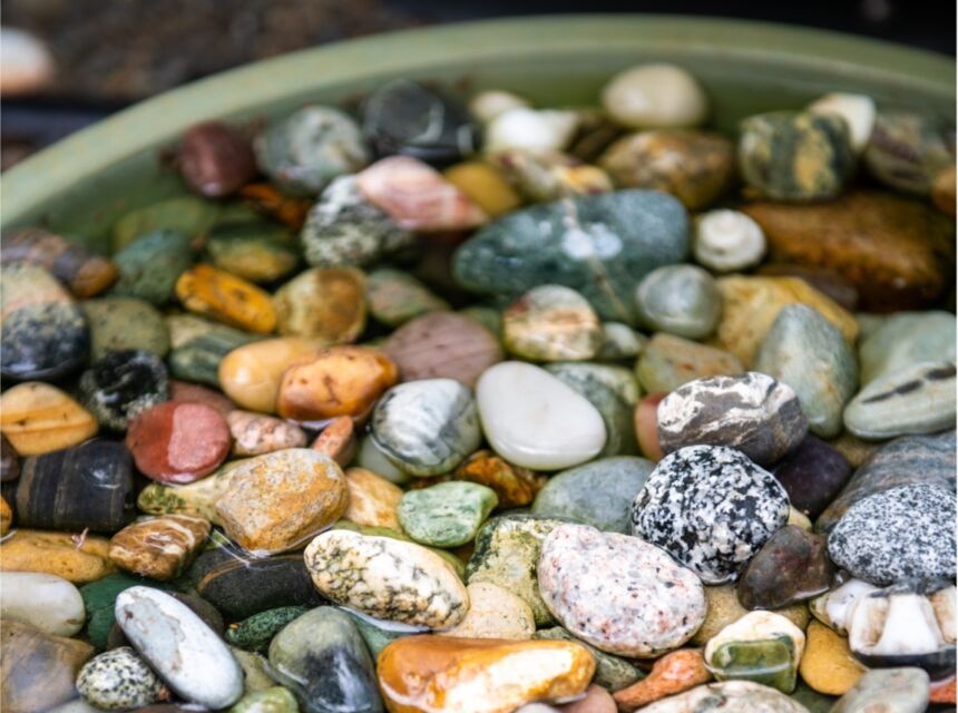 Shallow dish with many colorful pebbles and water, perfect for pollinators to drink from.